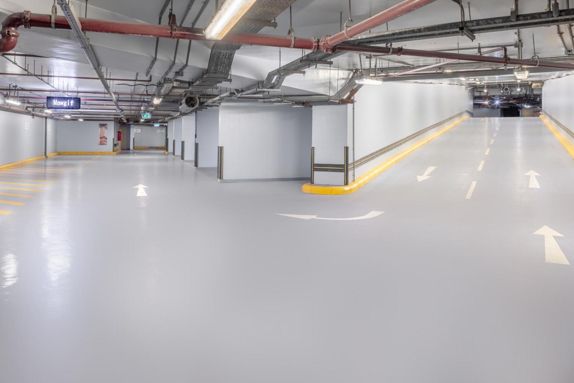 Jabal Omar Marriott Hotel Makkah Mecca Екстер'єр фото The photo shows a spacious underground parking garage with smooth, light gray flooring. The walls are primarily white, and there are exposed pipes running along the ceiling. There are directional arrows painted on the ground, indicating the flow of t